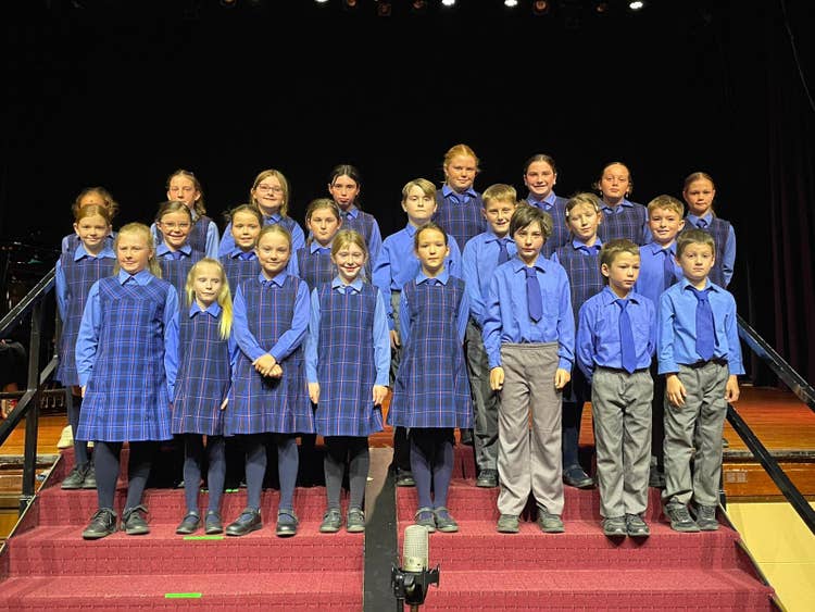 A group of students dressed in matching blue school uniforms are standing on a stage in neat rows, ready to perform or take part in a school event