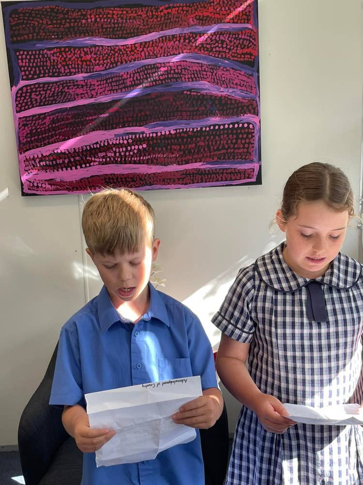 Two students stand in front of a wall art display, holding papers, as they participate in debating and public speaking activities.