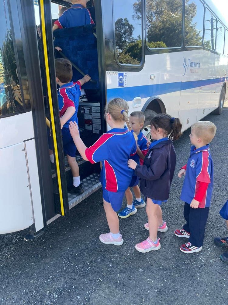 A group of students line up and board a bus for a school excursion, dressed in sports uniforms and preparing for a learning trip outside the classroom.